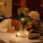 Two people sit at a table with flowers.