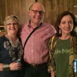 Three friends smiling with beers in hand.