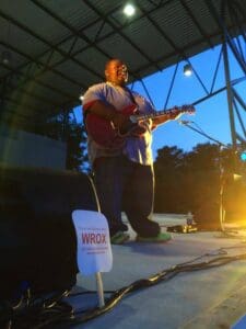 Man playing guitar on stage with WROX logo.