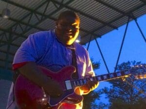 Man playing electric guitar outdoors.