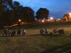 People sitting on chairs in grassy field.