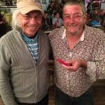 Two men smiling, one holding a red phone.