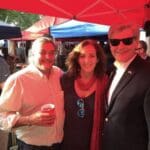 Three people smiling under a red tent.