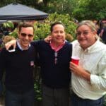 Three men smiling, one holding a red cup.