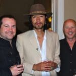 Three men smiling, one wearing a hat.