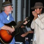 Man plays guitar while man plays harmonica.