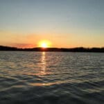 Sunset over a calm lake with trees in the background.