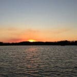 Sunset over a calm lake with trees in the distance.