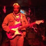 Man playing pink electric guitar on stage.