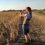 Woman in a field using binoculars.