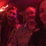 Three people smiling in a dimly lit room.