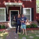 Two people stand in front of a red house.