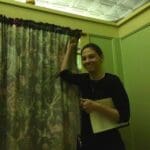 Woman holding a book by patterned curtain.