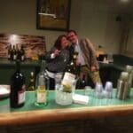Two people at a bar with wine and glasses.