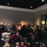 A group of people gather in a room with chairs.