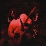 Man plays electric guitar in red light.