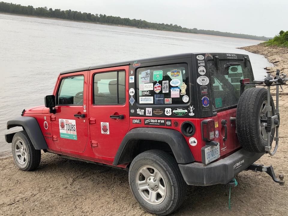 Red Jeep with stickers near a river.