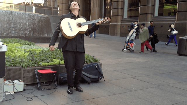 Guitarist performing outside in urban setting.