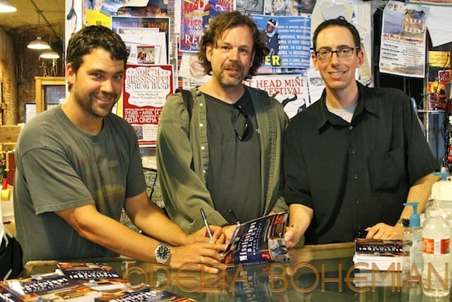 Three men signing books at a store.