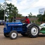 Man driving blue tractor with mower attachment.