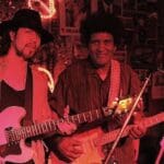 Two men playing guitars on stage.