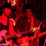 Two men playing guitars in a dimly lit room.