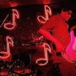 Man playing electric guitar in red light.