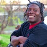 Smiling man with dreadlocks and black sweater.