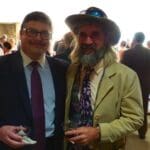 Two men in suits, one with a beard and hat.