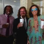 Three people pose, smiling and holding drinks.