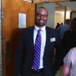 Man in suit with purple tie smiles at camera.