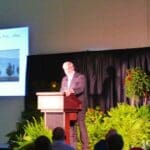 Man giving presentation at podium with screen behind him.