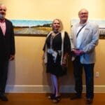 Three people stand in front of artwork.