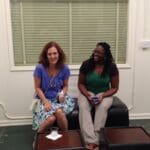 Two women smiling, sitting on a couch.