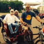 Three people riding a red tricycle and a bike.