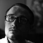 Man with glasses looking thoughtfully into distance.