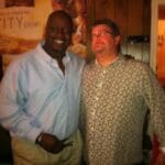 Two men smiling together in wood-paneled room